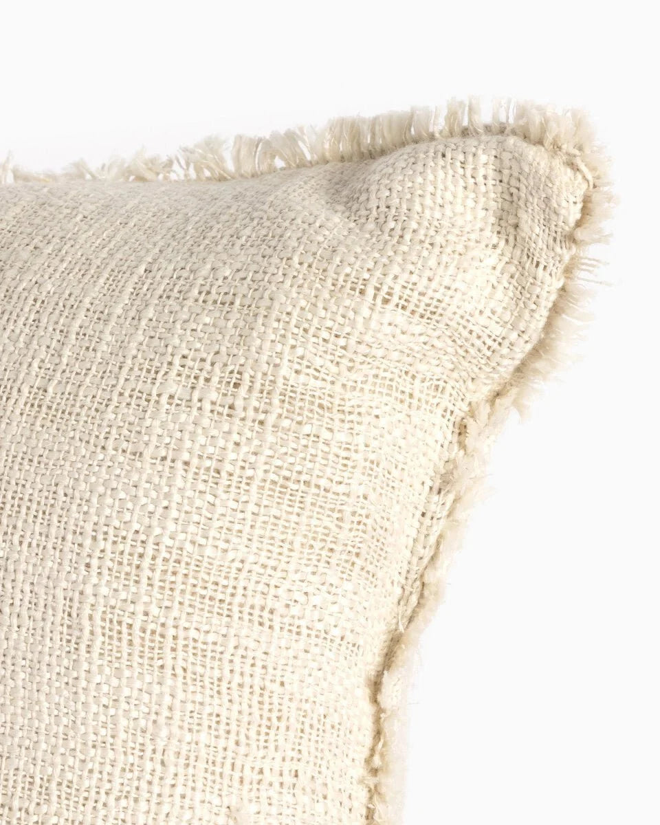 Cream textured outdoor pillow with fringe edges and woven fabric detail.